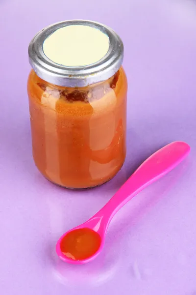 Color spoon for baby food with baby nutrition on purple background — Stock Photo, Image