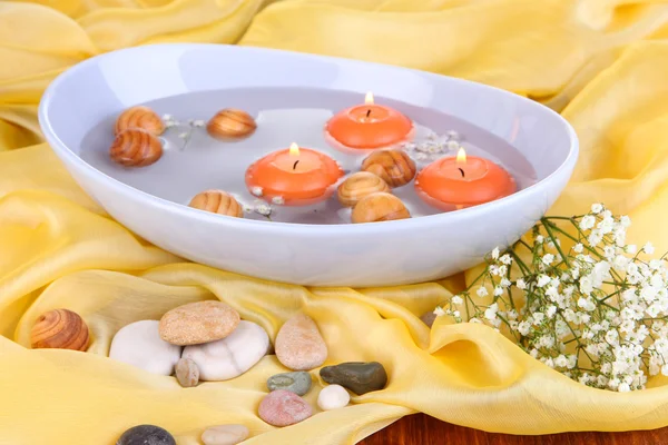 Beautiful candles swim in beautiful plate on yellow fabric close-up — Stock Photo, Image