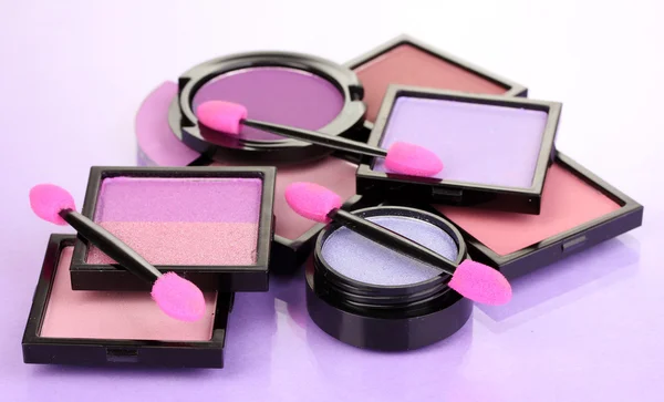 Brillantes sombras de ojos y cepillos de esponja para cimentar sobre fondo lila —  Fotos de Stock
