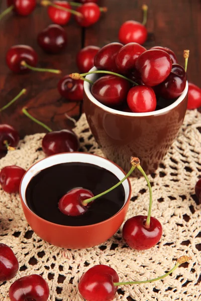 Спелые красные ягоды вишни в чашке и шоколадный соус на деревянном столе крупным планом — стоковое фото