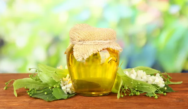 Tarro de miel con flores de lima, acacia sobre mesa de madera, sobre fondo brillante — Foto de Stock
