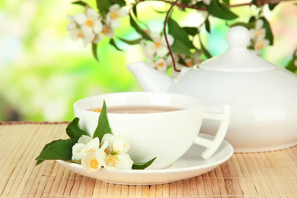 Taza de té con jazmín, sobre estera de bambú, sobre fondo brillante —  Fotos de Stock
