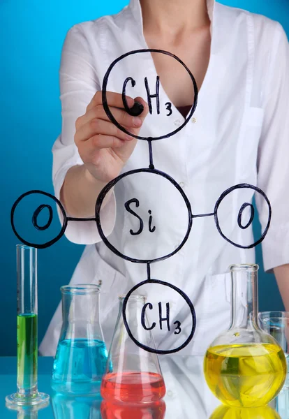 Chemist woman writing formulas on glass on blue background — Stock Photo, Image