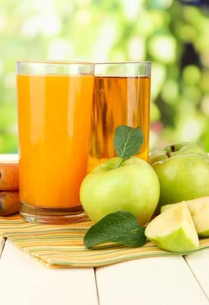 Glas juice, äpplen och morötter på vita träbord, på grön bakgrund — Stockfoto