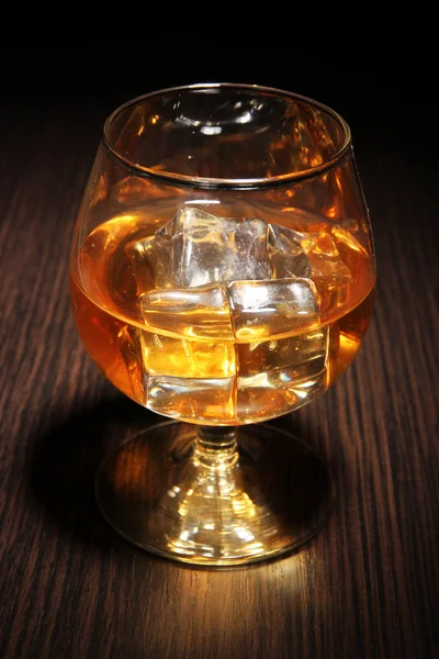 Brandy glass with ice on wooden background — Stock Photo, Image