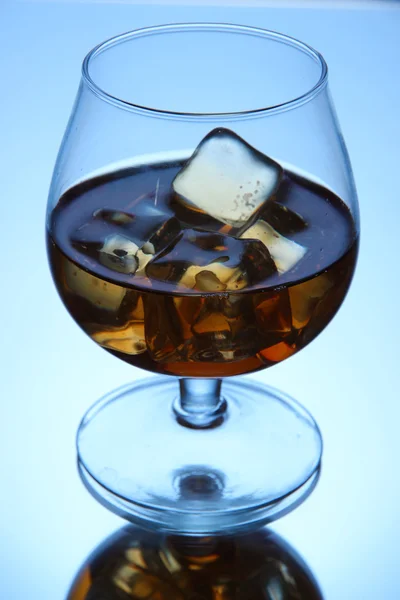 Brandy Glas mit Eis auf blauem Hintergrund — Stockfoto