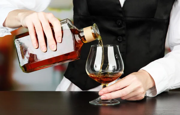 Бармен рука с бутылкой коньяка наливают напиток в стекло, на ярком фоне — стоковое фото