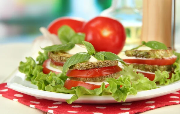 Tasty roasted marrow and tomato slices with salad leaves, on bright background — Stock Photo, Image