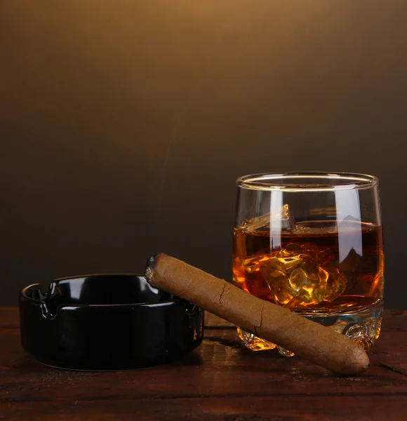 Bicchiere di brandy con ghiaccio e sigaro su tavolo di legno su sfondo marrone — Foto Stock