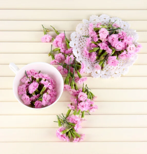 Muitos pequenos cravos cor-de-rosa no copo e no guardanapo no fundo de madeira — Fotografia de Stock