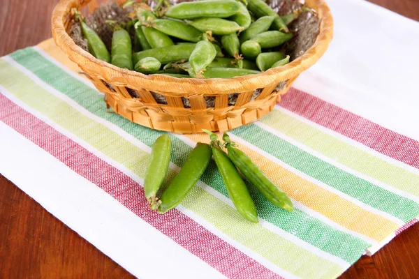 Green peas in wooden basket on napkin on table — Stock Photo, Image