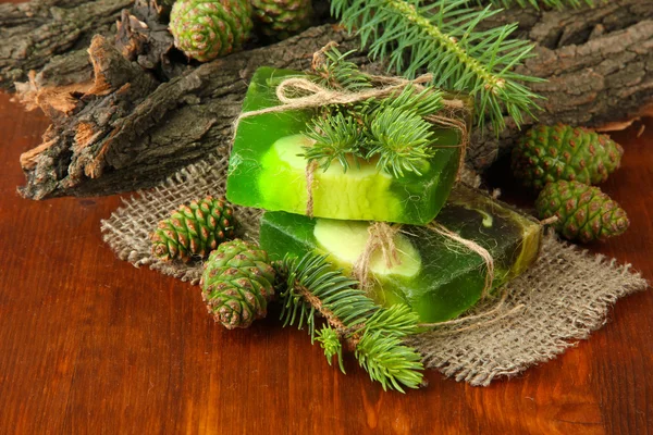 Jabón hecho a mano y conos de pino verde sobre mesa de madera — Foto de Stock