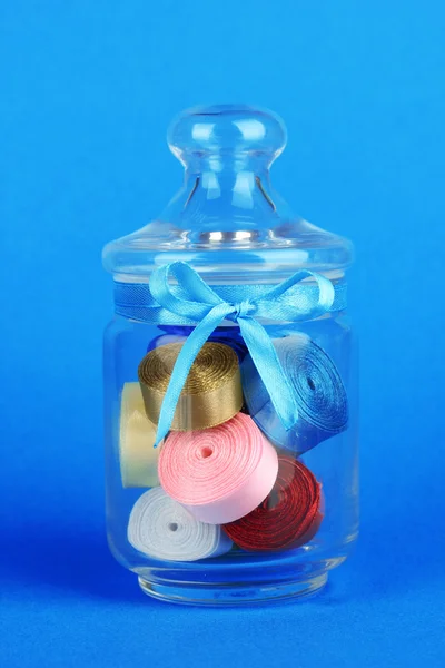Vaso di vetro contenente vari nastri colorati su sfondo blu — Foto Stock