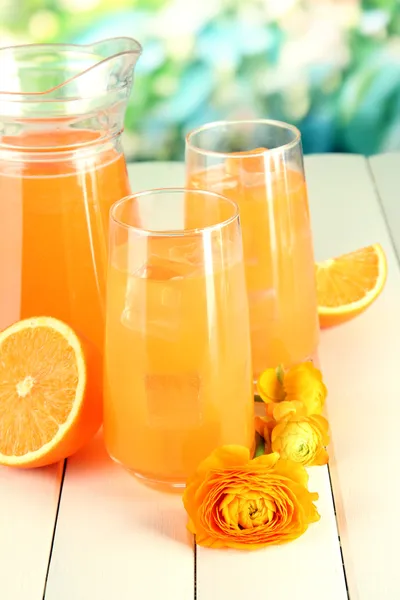 Gläser und Kanne Orangensaft auf Holztisch, auf grünem Hintergrund — Stockfoto