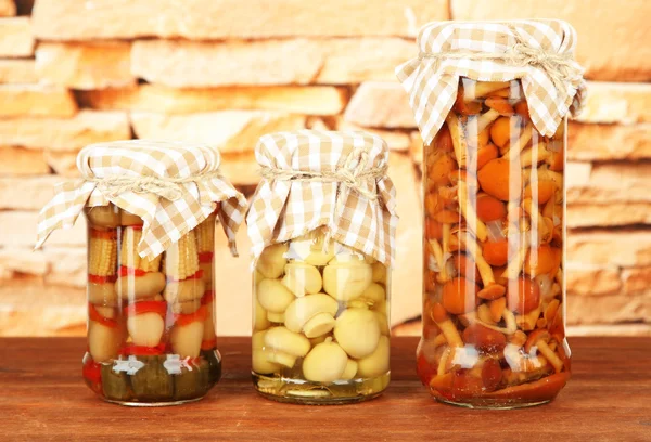 Delicious marinated mushrooms in glass jars, on wooden table on bright background — Stock Photo, Image