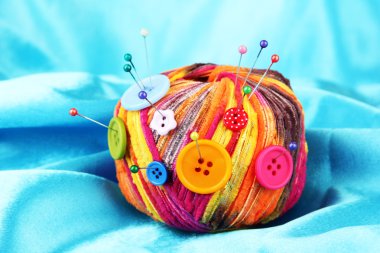 Colorful buttons and multicolor wool ball on color fabric background