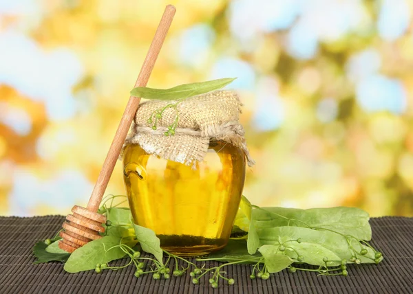 Tarro de miel con flores de lima, sobre estera de bambú de color sobre fondo brillante — Foto de Stock