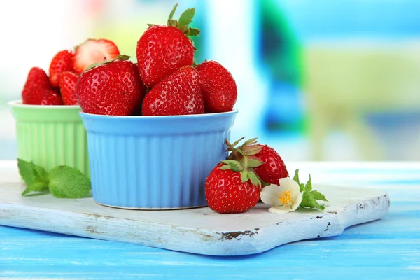 Rijpe zoete aardbeien in kommen op blauwe houten tafel — Stockfoto