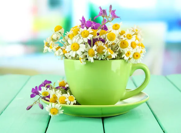 Bouquet of chamomile flowers in cup, on bright background — Stock Photo, Image