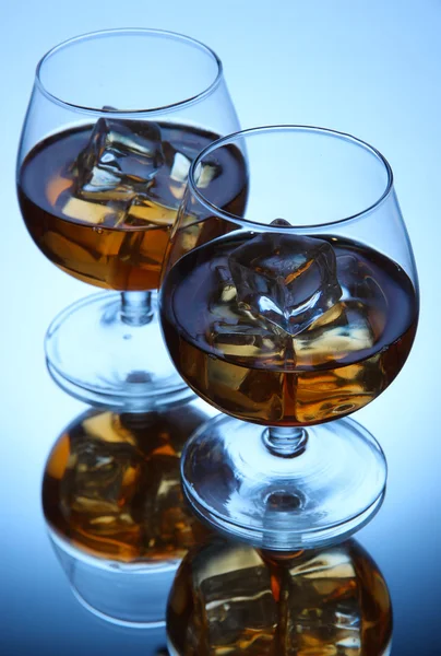 Brandy glasses with ice on blue background — Stock Photo, Image