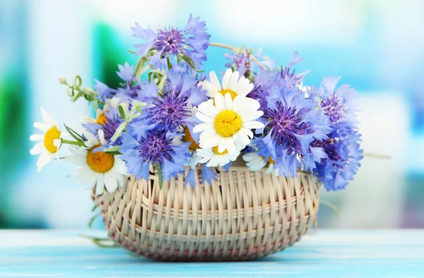 Schöner Strauß von Kornblumen und Kamillen im Korb auf blauem Hintergrund — Stockfoto