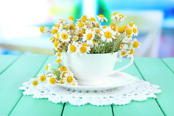 Bouquet of chamomile flowers in cup, on bright background — Stock Photo, Image