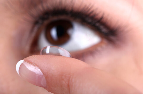 Young woman putting contact lens in her eye close up