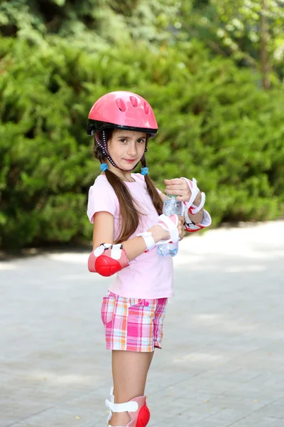 Девочка в роликовых коньках пьет воду в парке — стоковое фото