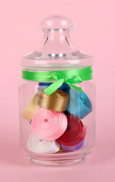 Vaso di vetro contenente vari nastri colorati su sfondo rosa — Foto Stock