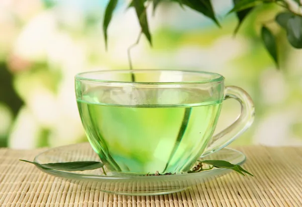 Transparante kopje groene thee op bamboe mat, op aard achtergrond — Stockfoto