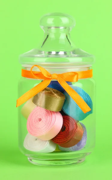 Glass jar containing various colored ribbons on green background — Stock Photo, Image