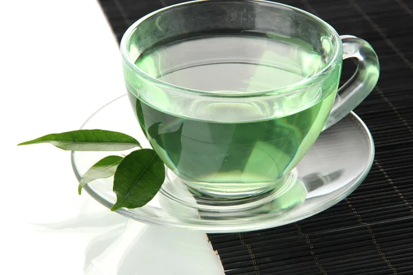 Taza transparente de té verde en estera de bambú, aislada en blanco — Foto de Stock