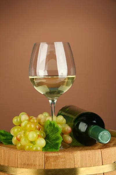 Composition of wine bottle, glass of white wine, grape on wooden barrel, on color background — Stock Photo, Image