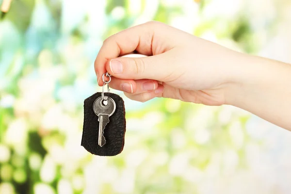 Key with leather trinket in hand on bright background