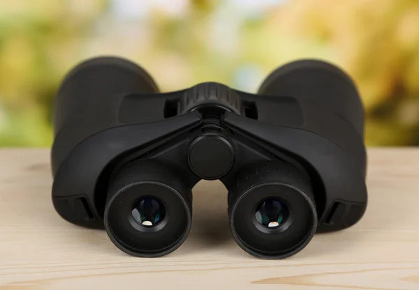 Black modern binoculars on wooden table on green background — Stock Photo, Image