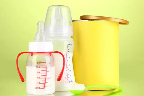 Bottles with milk and food for babies on green background — Stock Photo, Image