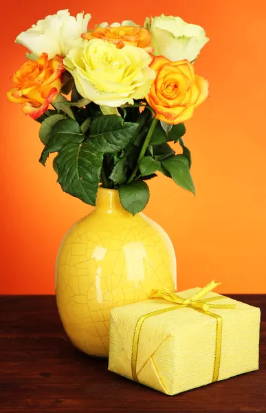 Beau bouquet de roses en vase avec cadeau sur table sur fond orange — Photo