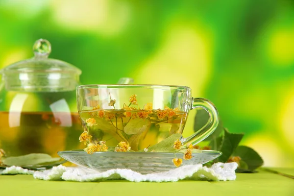 Kettle and cup of tea with linden on wooden table on nature background — Stock Photo, Image
