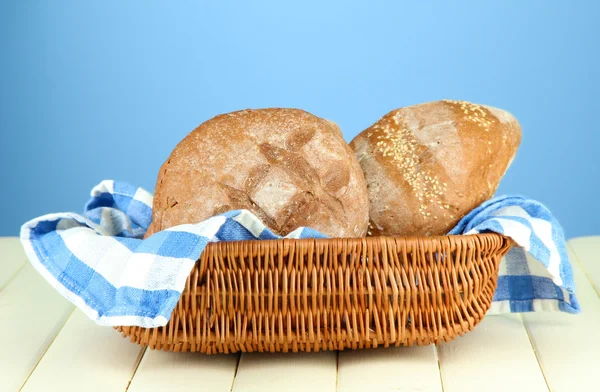 Bread in wicker basket, on wooden table, on color background — Stock Photo, Image