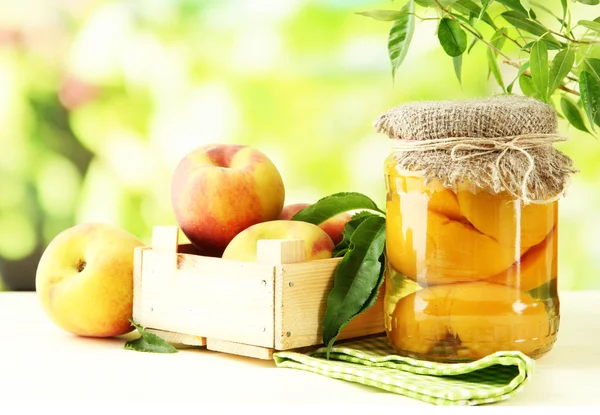 Jar of canned peaches and fresh peaches on wooden table, outside — Stock Photo, Image