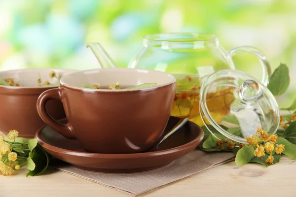 Hervidor de agua y taza de té con tilo sobre mesa de madera sobre fondo natural — Foto de Stock