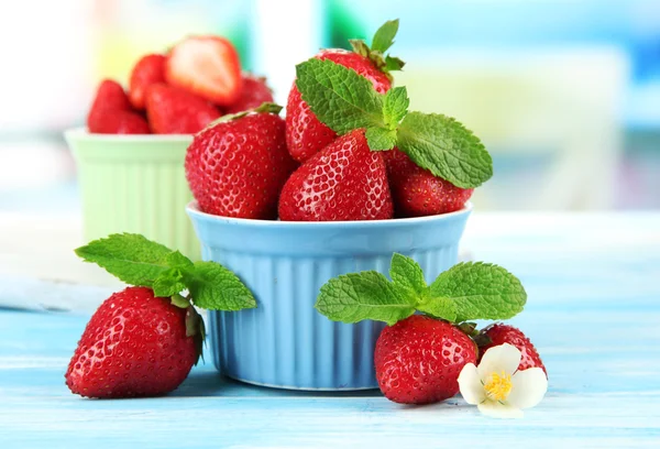 Ripe sweet strawberries in bowls on blue wooden table — Stock Photo, Image