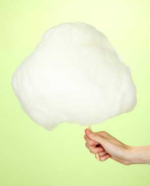 Hand holding stick with cotton candy, on color background clipart