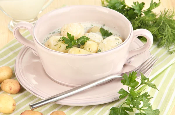 Tender young potatoes with sour cream and herbs in pan on wooden table close-up — Stock Photo, Image