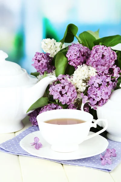 Sammansättning med vackra lila blommor, te service på träbord på ljus bakgrund — Stockfoto