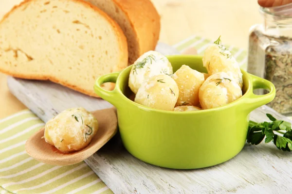 Inschrijving van jonge aardappelen met zure room en kruiden in pan op een houten bord op tabel close-up — Stockfoto