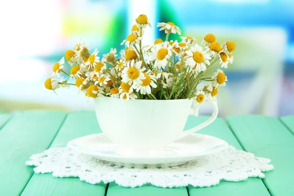 Bouquet of chamomile flowers in cup, on bright background — Stock Photo, Image