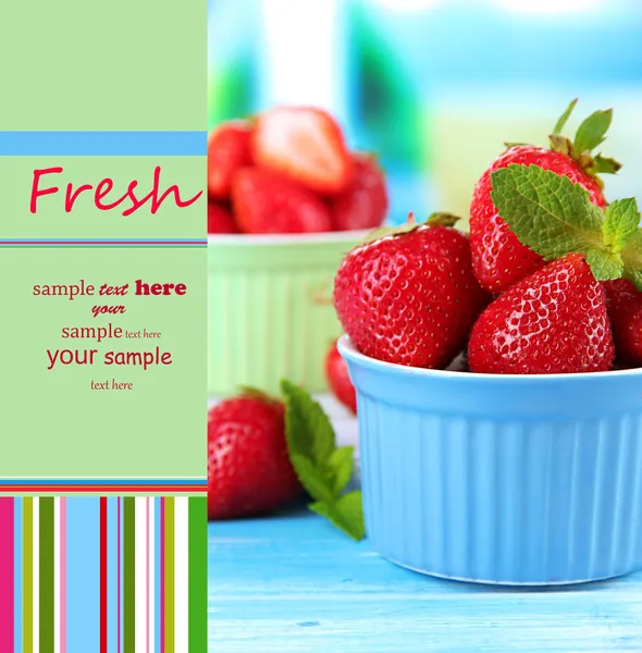Zralé sladké jahody v miskách na modré dřevěný stůl — Stock fotografie