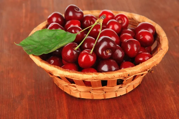 Cherry berries in wicker basket on wooden table close-up — Stock Photo, Image