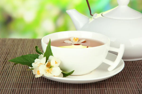 Чашка чая с жасмином, на бамбуковом коврике, на ярком фоне — стоковое фото